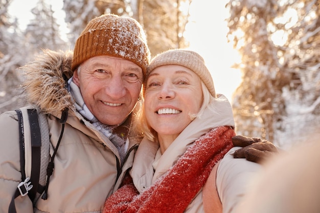 Pov ritratto di felice coppia senior che scatta foto selfie mentre si gode un'escursione nella foresta invernale