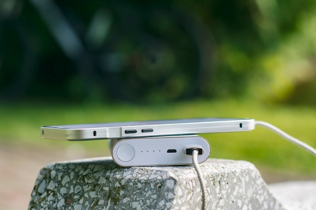 Power Bank carica uno smartphone su una panchina nel parco sullo sfondo di una bicicletta e alberi.