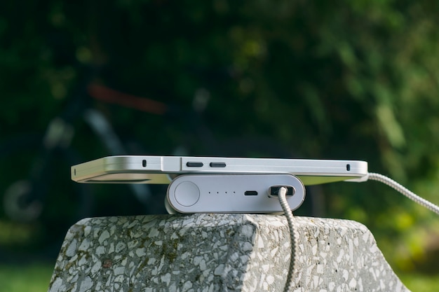 Power Bank carica uno smartphone su una panchina nel parco sullo sfondo di una bicicletta e alberi.