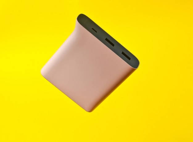 Power bank colore rosa pallido su uno sfondo giallo. Batteria esterna per gadget. Levitazione di oggetti.