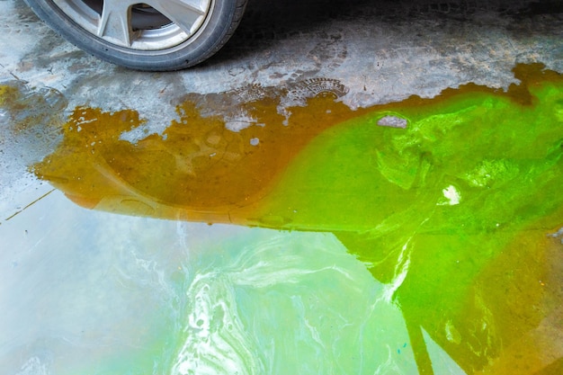Pozza di liquido di raffreddamento verde e liquidi tecnici marroni sul pavimento di cemento vicino all'auto