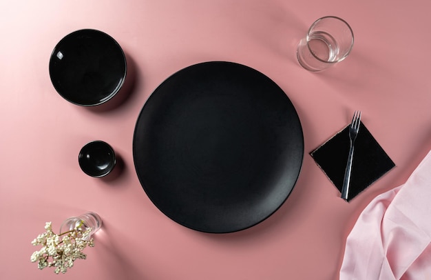 Pranzo allestito con piatto nero vuoto posizionato su sfondo rosa