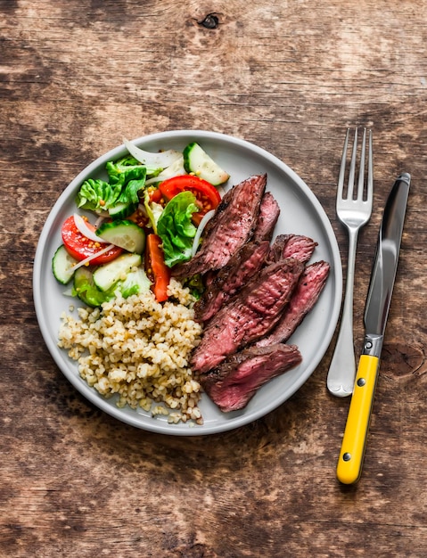 Pranzo delizioso bulgur insalata di verdure fresche e bistecca su uno sfondo di legno vista dall'alto