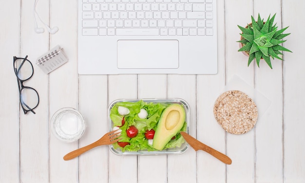 Pranzo fatto in casa vegano sano in scatola di pranzo sul tavolo di legno bianco con calendario delle cuffie del computer portatile