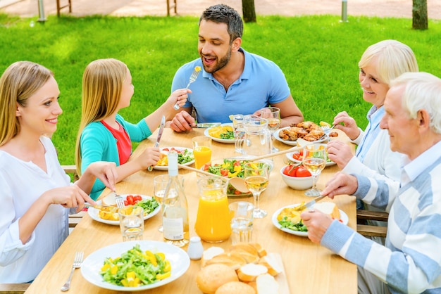 Pranzo in famiglia insieme. Vista dall'alto di una famiglia felice di cinque persone che comunicano e si godono il pasto insieme seduti al tavolo da pranzo all'aperto