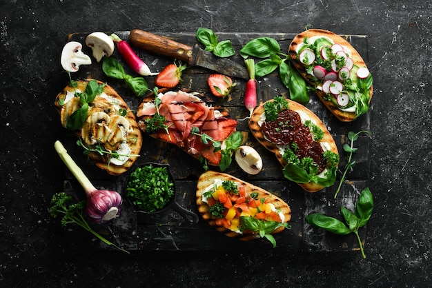 Pranzo Panini fatti in casa con pomodori prosciutto crudo verdure e formaggio su sfondo di pietra nera Bruschetta Vista dall'alto