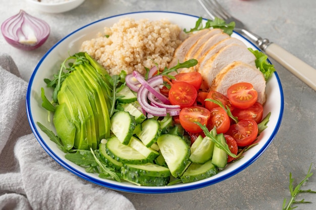 Pranzo salutare con pollo alla griglia, quinoa, avocado, pomodori, cetrioli e rucola fresca