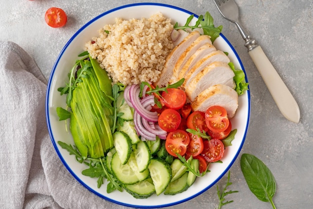 Pranzo salutare con pollo alla griglia, quinoa, avocado, pomodori, cetrioli e rucola fresca