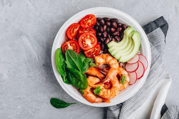 Pranzo sano a base di pesce Gamberetti speziati Burrito Buddha Ciotola con riso selvatico, spinaci, pomodori, ravanello, fagioli neri e avocado