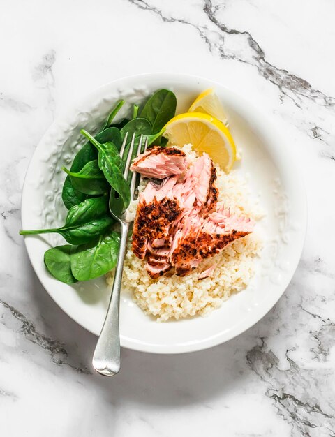 Pranzo sano couscous al limone salmone grigliato e spinaci freschi su uno sfondo di marmo chiaro vista dall'alto