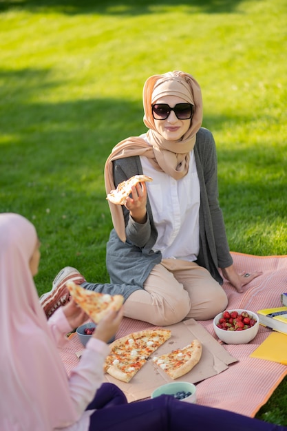 Pranzo squisito all'aperto. Donna musulmana che indossa occhiali da sole mentre pranza fuori con un amico