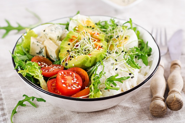 pranzo vegetariano ciotola di buddha con uova, riso, pomodoro, avocado e gorgonzola sul tavolo.