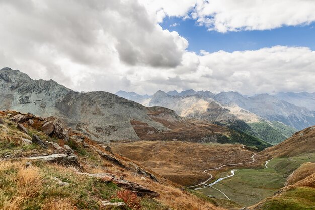 Prati alpini colorati all'inizio dell'autunno con rocce ripide sul flusso d'acqua all'orizzonte e percorso di trekking