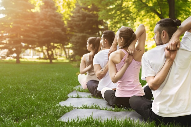 Pratica di yoga di gruppo, gente sportiva che si allena nella posa della testa di mucca, facendo schiena e spalle che si allungano nel parco, vista posteriore, spazio copia