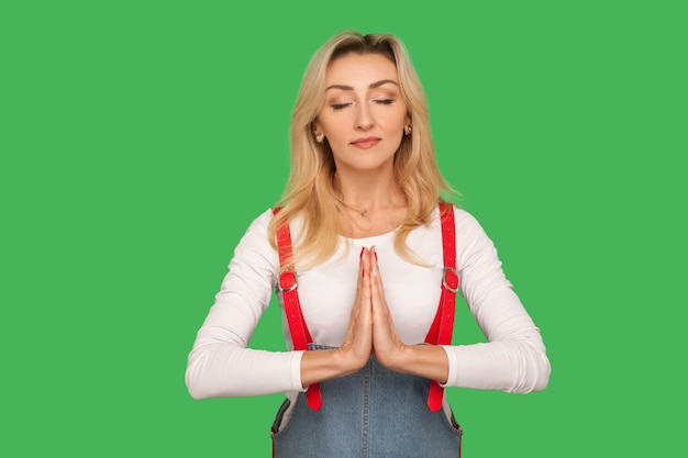 Pratica yoga mente pacifica Ritratto di bella donna adulta calma in tuta elegante meditando con gesto namaste sentendosi concentrato e rilassato girato in studio isolato su sfondo verde