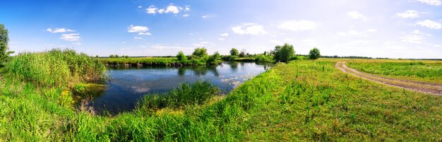 Prato con il fiume e la strada campestre sotto cielo blu