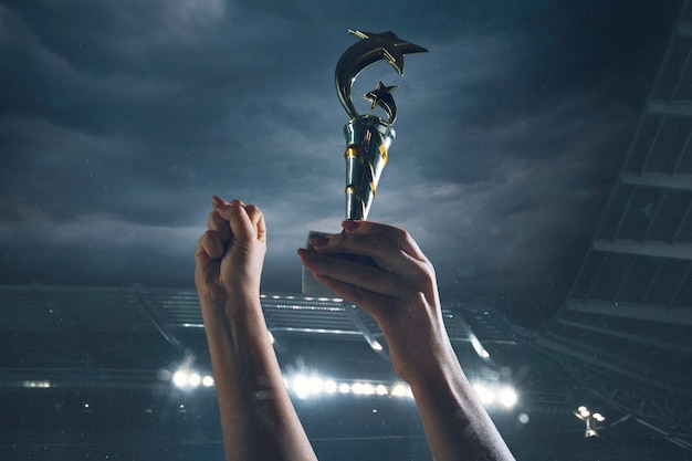 Premio della vittoria, mani maschili che stringono la coppa dei vincitori contro il cielo nuvoloso scuro
