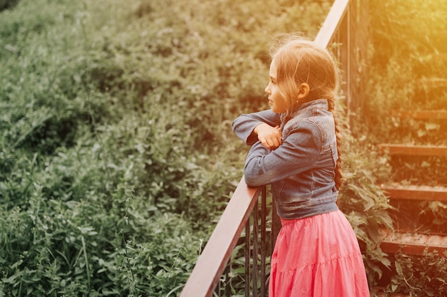 Premurosa candida bambina di otto anni si trova su una scala con erba e si gode la natura età prepuberale dei bambini e le loro vite psicologia mentale e concetto di salute mentale bagliore