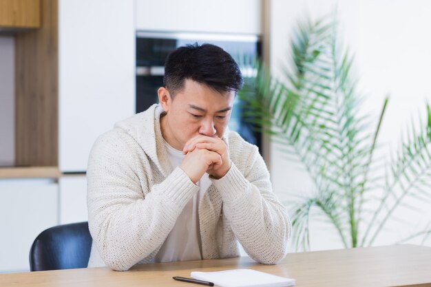 premuroso serio giovane uomo asiatico che guarda lontano studente scrittore seduto a casa scrivania dell'ufficio con laptop