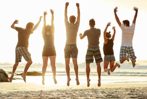 Prendere l'aria in spiaggia Ripresa di un gruppo di amici non identificabili che saltano insieme sulla spiaggia al tramonto