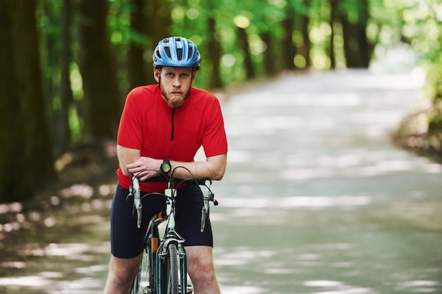Prendere una pausa. Il ciclista su una bici è sulla strada asfaltata nella foresta alla giornata di sole