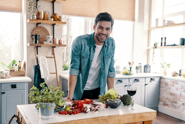 Prendersi cura della sua salute. Bel giovane in abbigliamento casual che guarda la macchina fotografica e sorride mentre si trova in cucina a casa