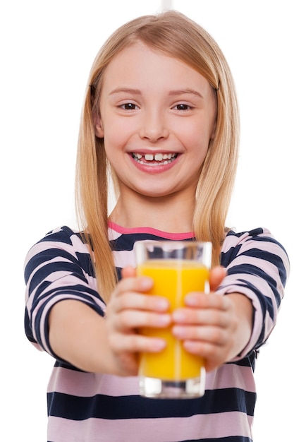 Prendi un succo! Bambina allegra che allunga le mani con un bicchiere di succo d'arancia e sorride alla telecamera mentre si trova isolata su bianco