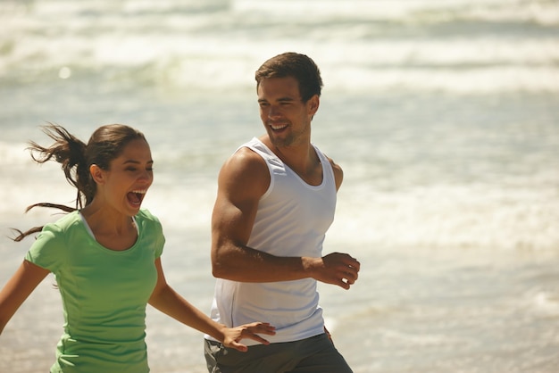 Prendimi se puoi Inquadratura di una giovane coppia ridente che fa jogging insieme sulla spiaggia