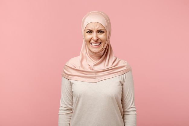 Preoccupata e dispiaciuta giovane donna musulmana araba in abiti leggeri hijab in posa isolata su sfondo rosa in studio. Concetto di stile di vita dell'Islam religioso della gente. Mock up spazio di copia. Piangere, guardare la fotocamera.