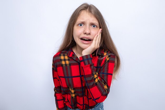 Preoccupato per mettere la mano sulla guancia bella bambina che indossa una camicia rossa isolata sul muro bianco