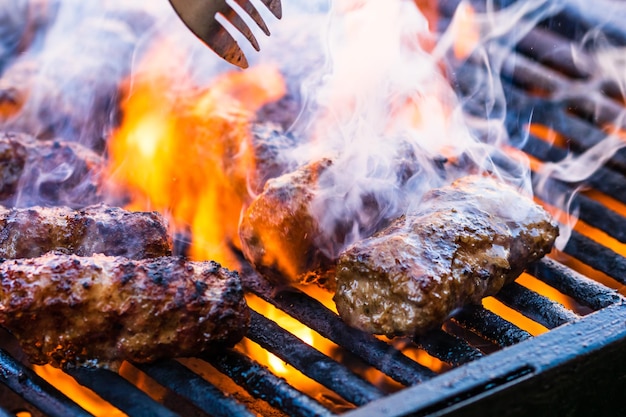 Preparare al barbecue involtini di carne chiamati mici o mititei. primo piano della griglia con fuoco ardente con fiamma e fumo.