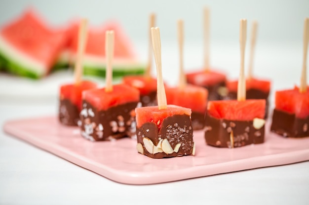 Preparare antipasti di anguria immersi nel cioccolato e spolverati con sale marino e mandorle.