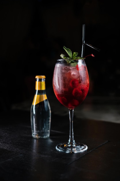 Preparare cocktail a casa come un esperto barman di una discoteca Cocktail fatti in casa colorati freschi e succosi guarniti con frutti di bosco, menta arancione su sfondo scuro Bottiglia di soda dietro