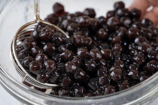 Preparare il tè a bolle, raccogliere e versare le palline di bolla di perle di tapioca al sapore di zucchero di canna cotto nella tazza su sfondo bianco tavolo in legno, primo piano, copia spazio.