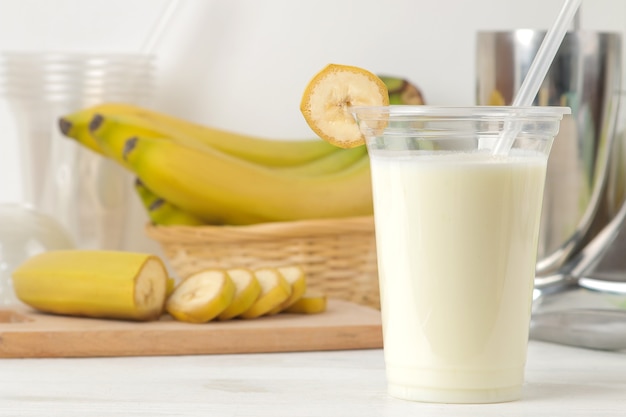 Preparare un frullato. bicchiere di plastica usa e getta con frullato di banana, ingredienti per cucinare e mixer