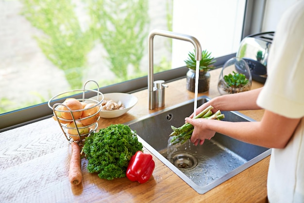 Preparare un pasto delizioso Foto ritagliata di una donna che lava le verdure in un lavello da cucina