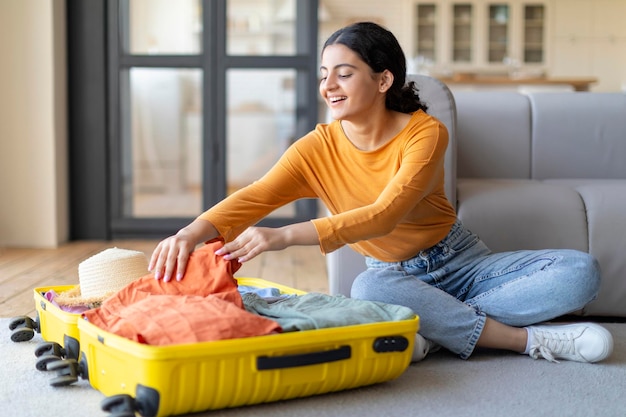 Prepararsi per il viaggio allegra giovane donna indiana che prepara la valigia a casa