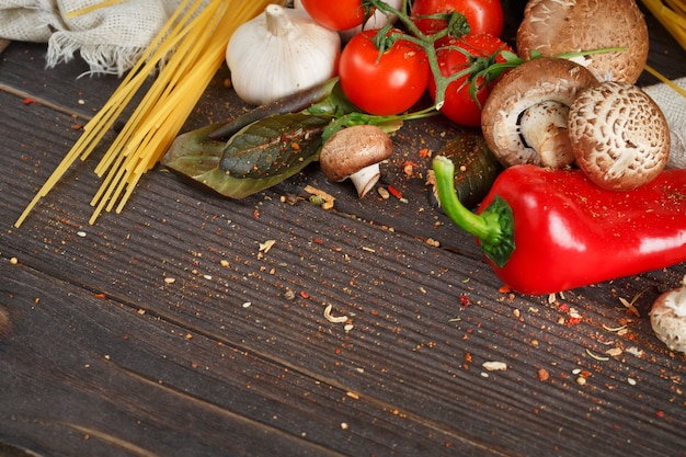 Preparazione degli spaghetti con pomodori, aglio, funghi, pepe e olio d'oliva, su tavola di legno