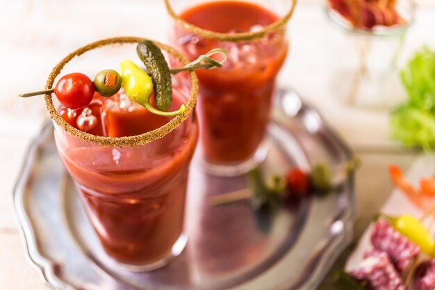 Preparazione del cocktail di bloody mary guarnito con coste di sedano, olive e striscioline di pancetta.