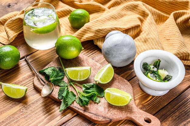 Preparazione del cocktail Mojito. Ingredienti Menta, lime, ghiaccio e utensili da bar. Fondo in legno. Vista dall'alto.