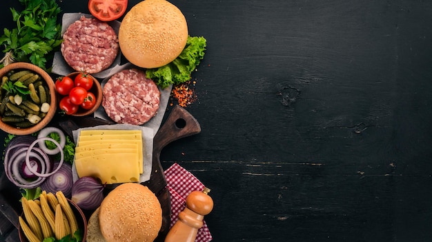 Preparazione dell'hamburger Carne verdure fresche pomodori cipolle Su uno sfondo di legno nero Vista dall'alto Spazio libero per la copia