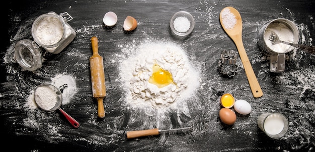 Preparazione dell'impasto. Ingredienti per la pasta - Farina, uova e attrezzi - mattarello, setaccio, frusta. Su uno sfondo di legno nero. Vista dall'alto