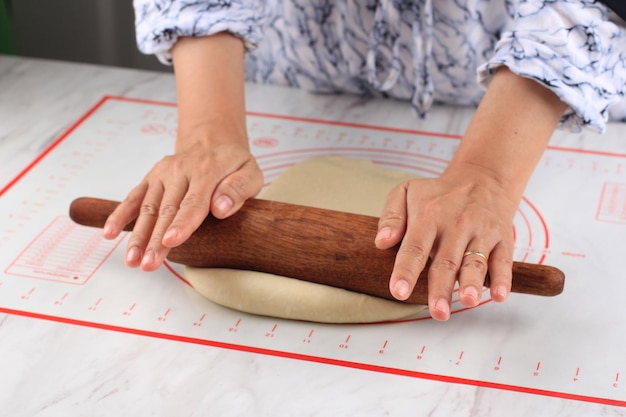 Preparazione dell'impasto. Le mani delle donne che rotolano la pasta con il mattarello