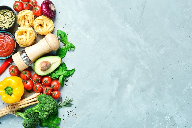 Preparazione della pasta Pasta secca e ingredienti pomodori basilico pepe e rosmarino su fondo di pietra grigia Pasta secca Vista dall'alto Spazio libero per il testo