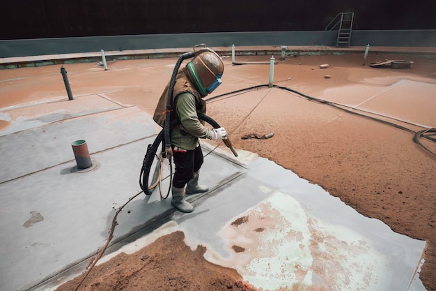 Preparazione della piastra di corrosione della superficie del lavoratore maschio mediante sabbiatura rimbalzo dal ponte superiore del serbatoio