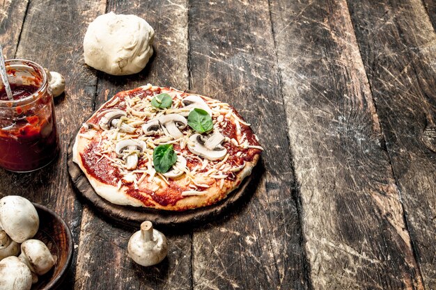 Preparazione della pizza con ingredienti naturali. Su uno sfondo di legno.