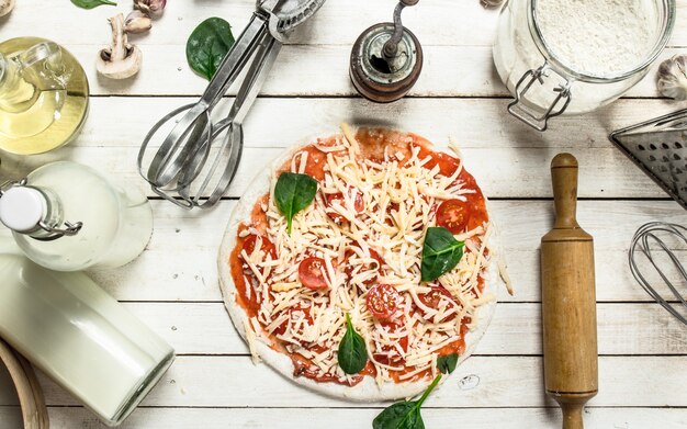 Preparazione della pizza con vari ingredienti. Su un tavolo di legno bianco.