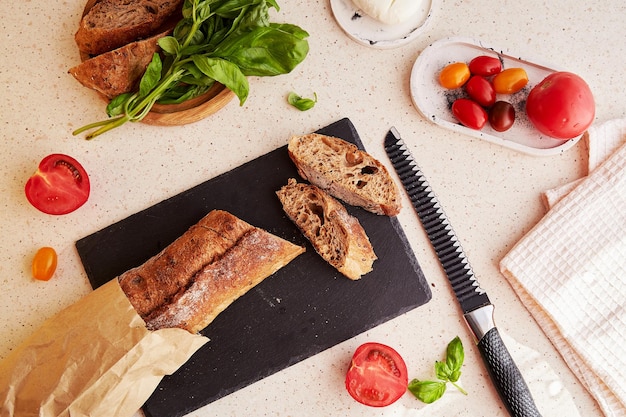 Preparazione della tradizionale insalata caprese con pomodori freschi basilico mozzarella e baguette sulla superficie di marmo Insalata rustica naturale Vista dall'alto cibo