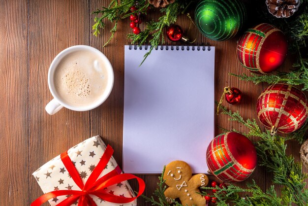 Preparazione delle vacanze invernali di Natale e Capodanno, pianificazione di un accogliente sfondo in legno con scatola regalo di blocco note vuoto, nastro rosso, tazza di latte o cacao, rami di abete e palline di Natale, spazio per la copia