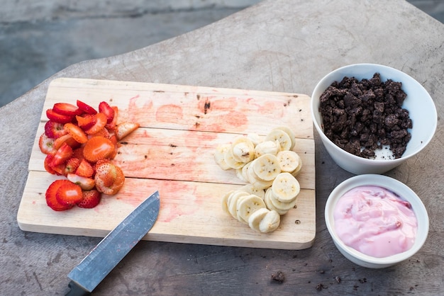 Preparazione di cibi dolci con Banana Fragola Cacao e Yogurt su tavola di legno